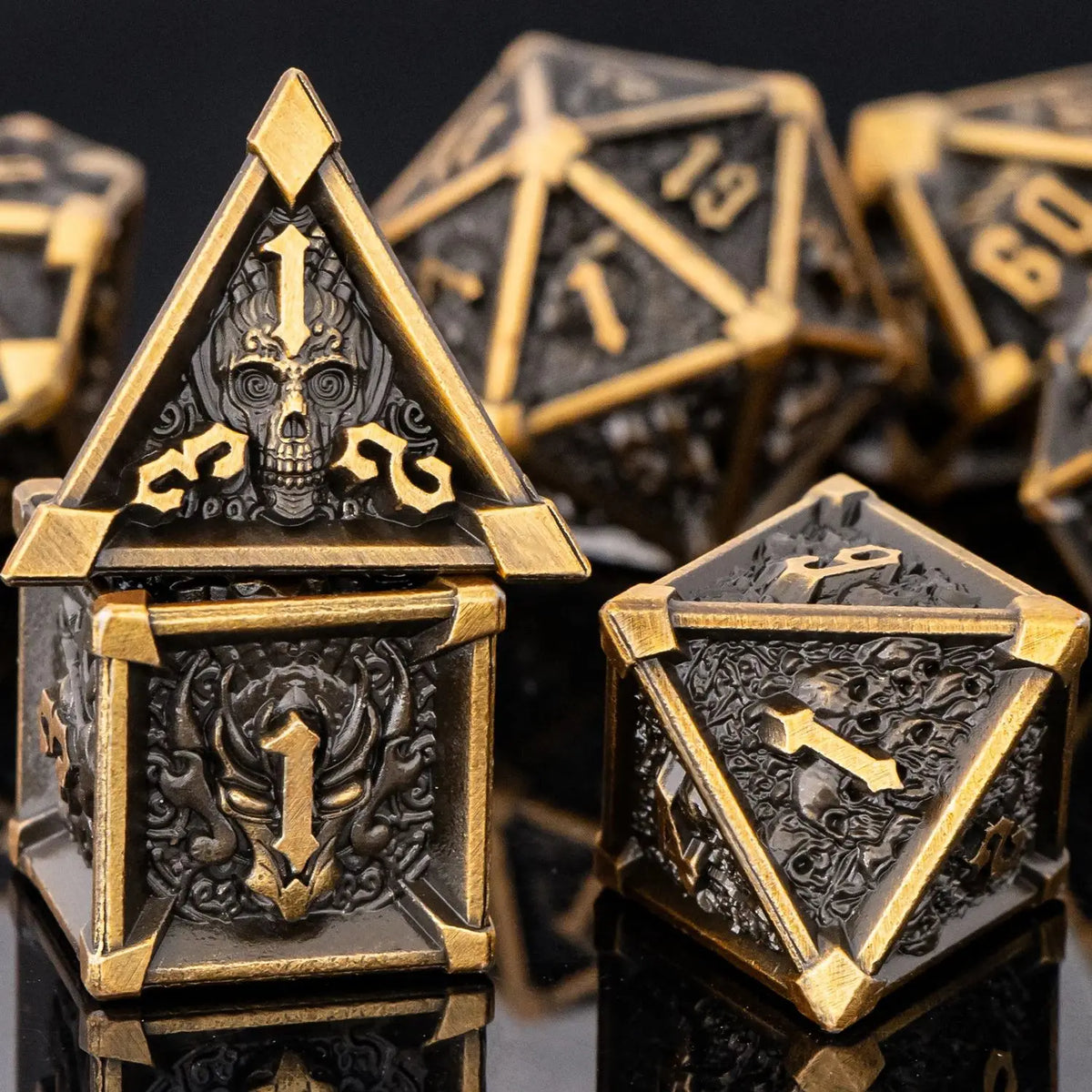 A close-up of a set of seven gold and dark metal dice, including a pyramid die, resting on a reflective surface.