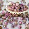 A pile of vibrant round beads in pink and gold tones is displayed in a white bowl.