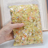 A hand holds a clear plastic bag filled with multicolor aurora resin nail charms.