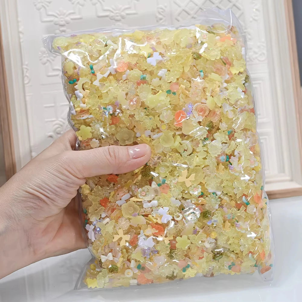 A hand holds a clear plastic bag filled with multicolor aurora resin nail charms.