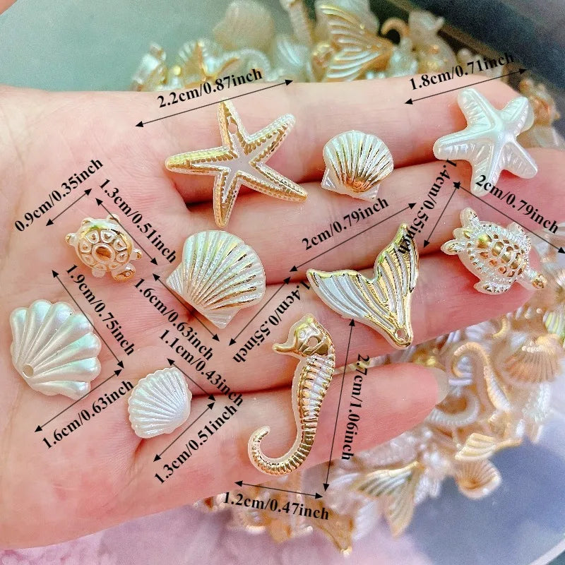 A hand displays various gold and white acrylic ocean animal beads including starfish, shells, and a seahorse.