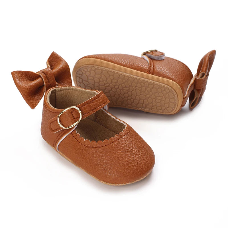 A pair of brown lace-trimmed baby girl moccasin shoes with bows shown from the side.
