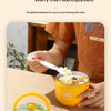 A hand is holding a yellow insulated stainless steel breakfast cup with a lid on a wooden table.
