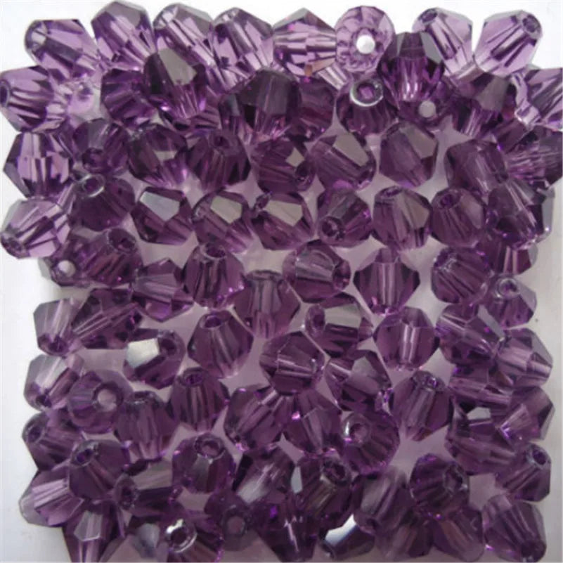 A close-up view of small, faceted purple glass bicone beads for jewelry making.
