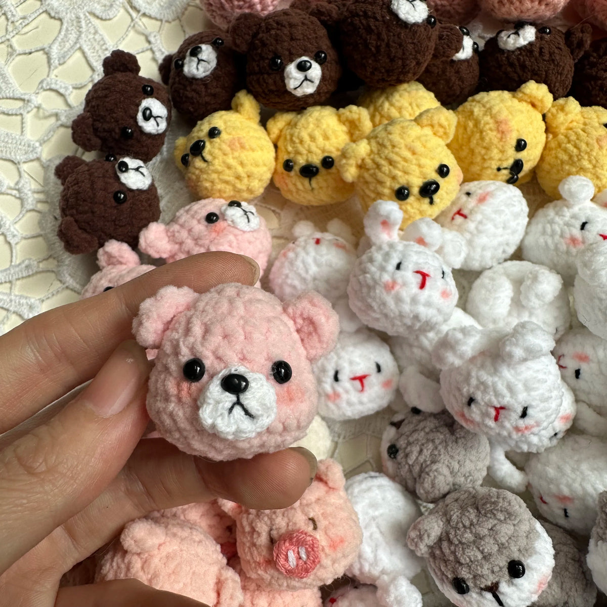 A hand holds a collection of handcrafted crochet animal keychains including rabbits, chicks, and bears in various colors.