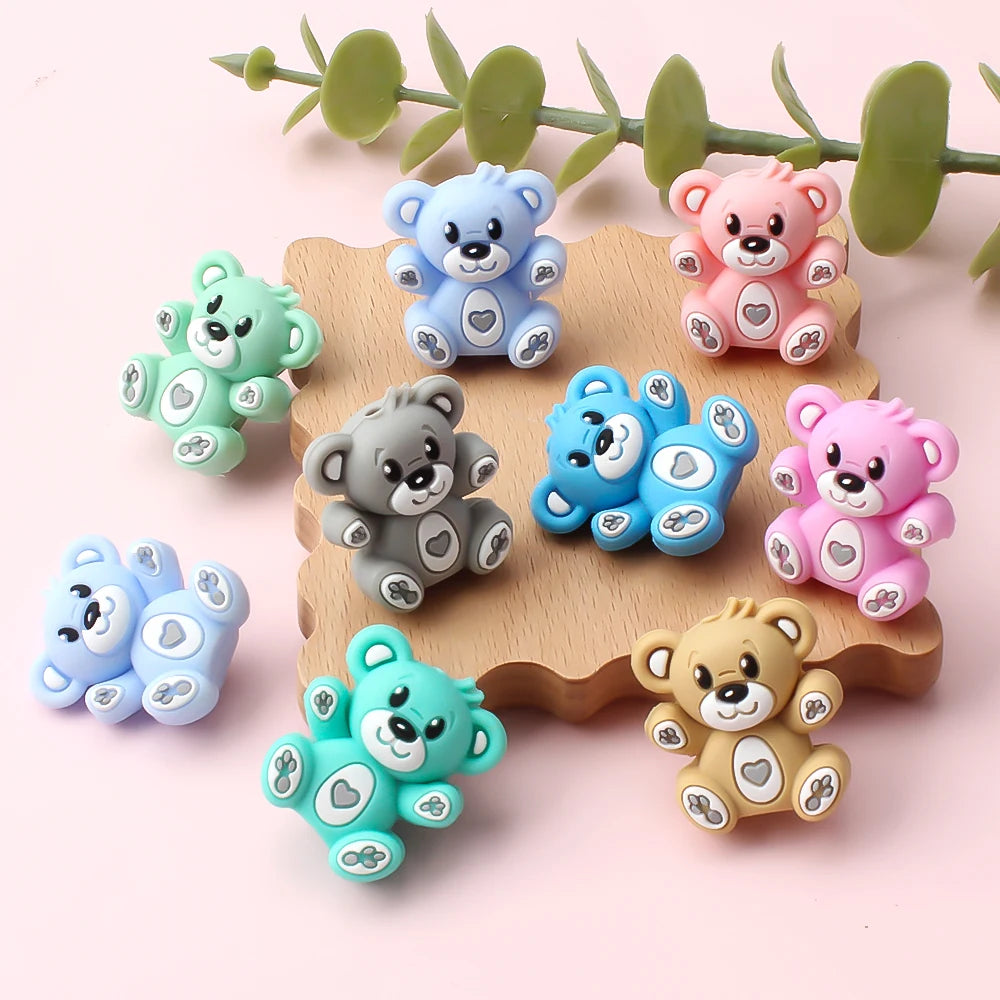 A collection of colorful 3D silicone bear focal beads in various pastel colors arranged on a wooden surface.