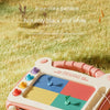 A pink magnetic drawing board with colorful shapes and a purple pencil lying on green grass.