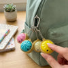 A hand holds a set of yellow and green dumpling squishy keychains attached to a zipper pull on a green fabric bag.