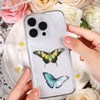 A hand holds a clear phone case featuring a black and yellow butterfly design against a white background, surrounded by light