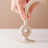 A hand is holding a smooth, beige silicone teething toy with a looped handle and a round base.