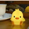 A glowing yellow cartoon duck night light sitting on a wooden surface next to a white bowl.