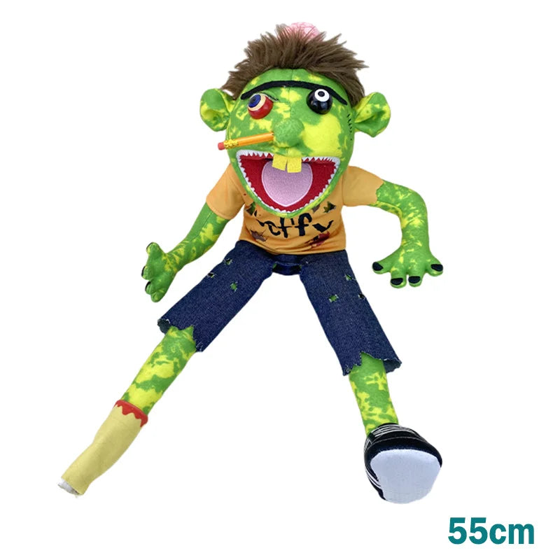 A green, furry hand puppet with large eyes and a mouth showing teeth, wearing an orange shirt and blue pants.