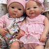 A realistic soft silicone reborn baby doll with a pink outfit is shown lying down.