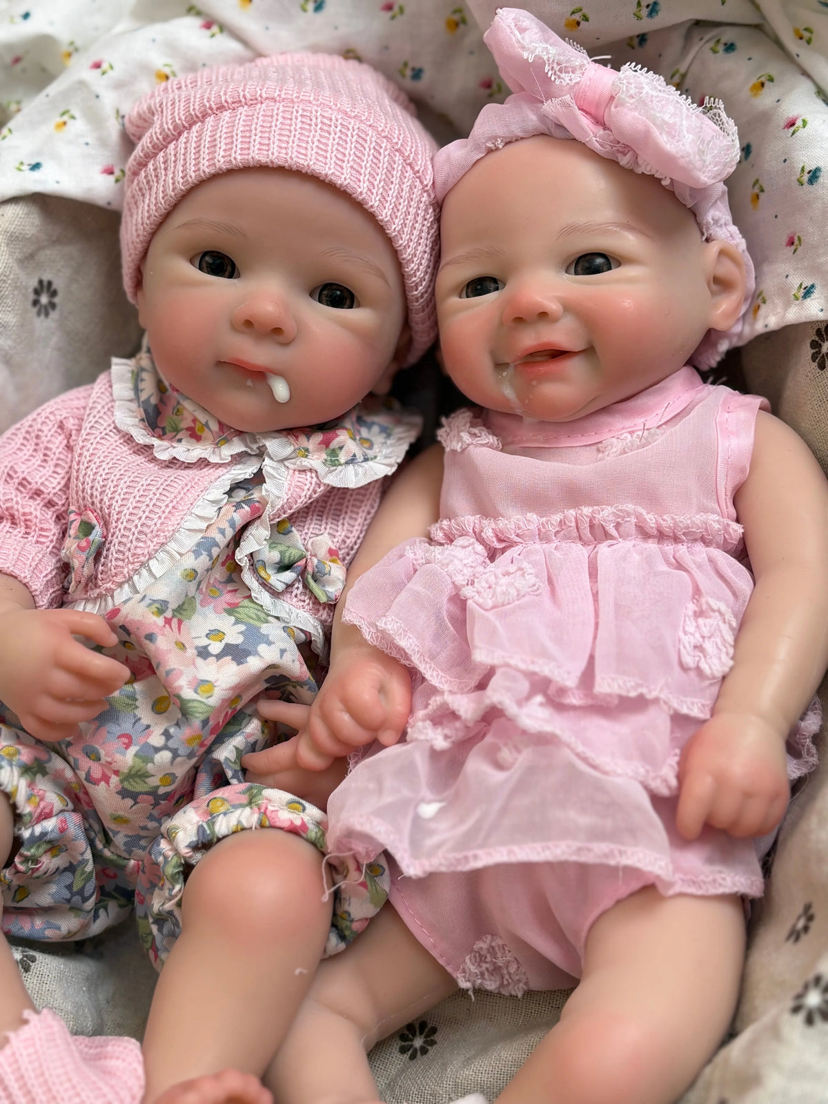 A realistic soft silicone reborn baby doll with a pink outfit is shown lying down.