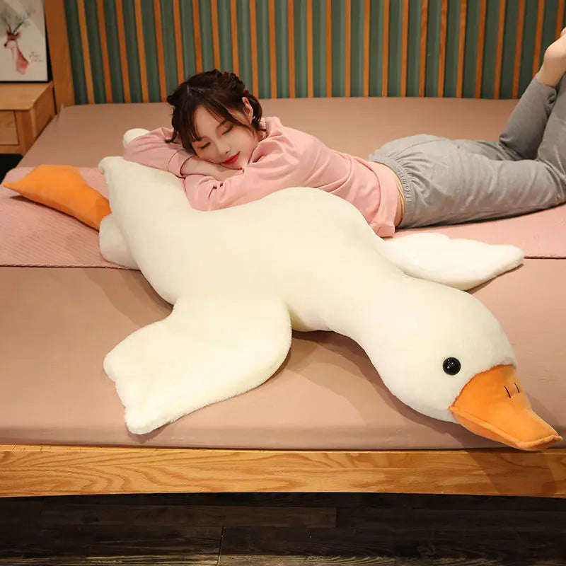 A person is relaxing on a pink surface with an extra-large white plush goose pillow.
