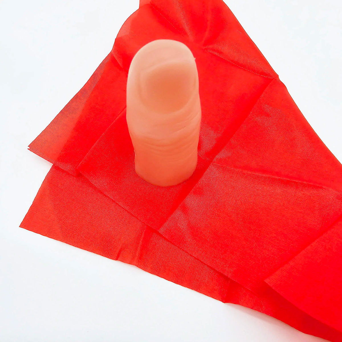 Un doigt rose de rechange est posé sur un tissu de soie rouge pour un tour de magie.