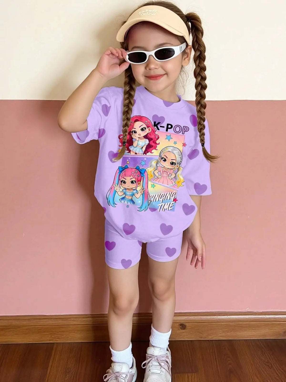 A young girl wearing a purple t-shirt and shorts with K-Pop and singing time graphics, standing against a pink wall.