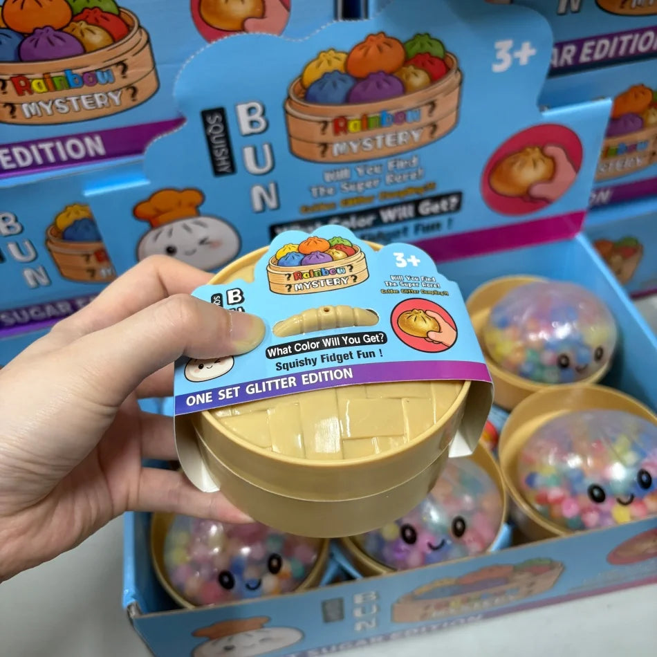 Une main tient un jouet anti-stress en forme de dumpling de perles arc-en-ciel jaune dans sa boîte.