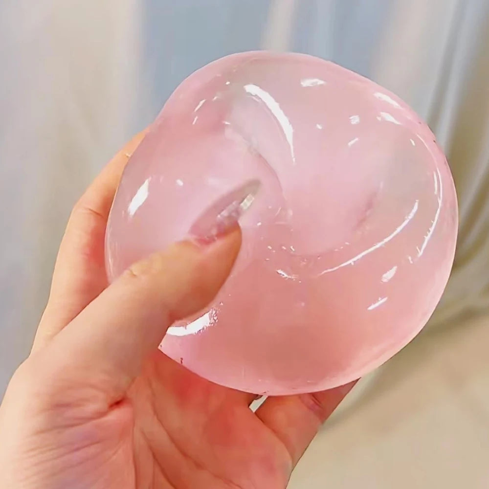 A hand holds a translucent pink squishy stress relief toy, showing its smooth texture and rounded shape.