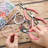 A hand is using pliers and nippers to work on beads and wire within a clear storage box.
