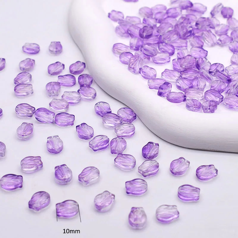 A collection of purple gradient glass beads is displayed next to a white tool, showing various sizes and shapes for jewelry m