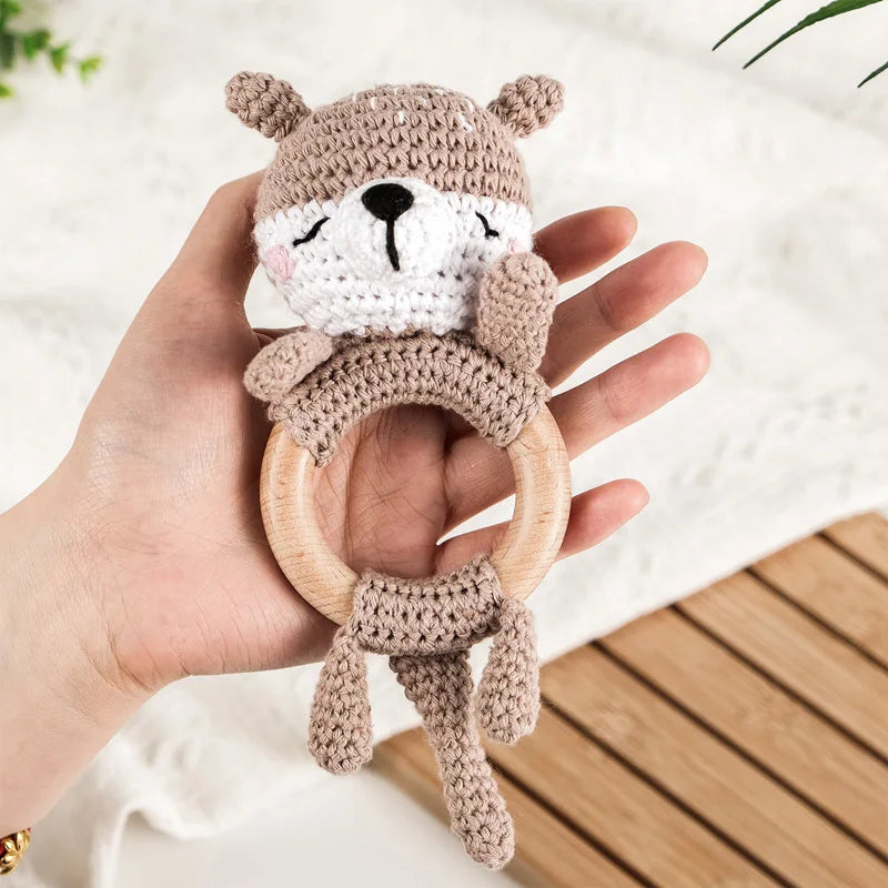 A hand holds a knitted brown bear rattle and teether ring made of wood