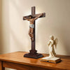 A wooden crucifix with a figure of Jesus, standing on a brown base next to an open book.