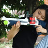 A young woman holds a white and black soft bullet shotgun toy with red shells, outdoors.