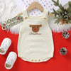 A cream-colored baby Christmas romper with a brown Santa embroidery, displayed on a wooden hanger against a red background.
