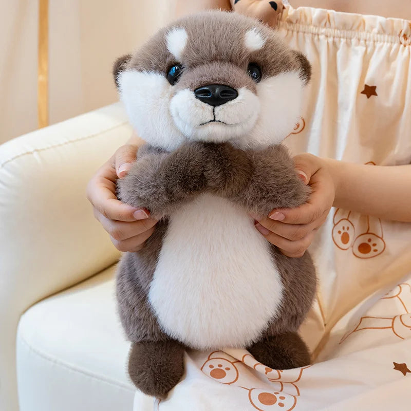 A soft, gray and white magnetic otter plush toy is being held by a person in a light-colored setting.