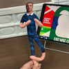 A man is holding a stuffed doll resembling Erling Haaland with flexible joints next to a sign displaying national flags.