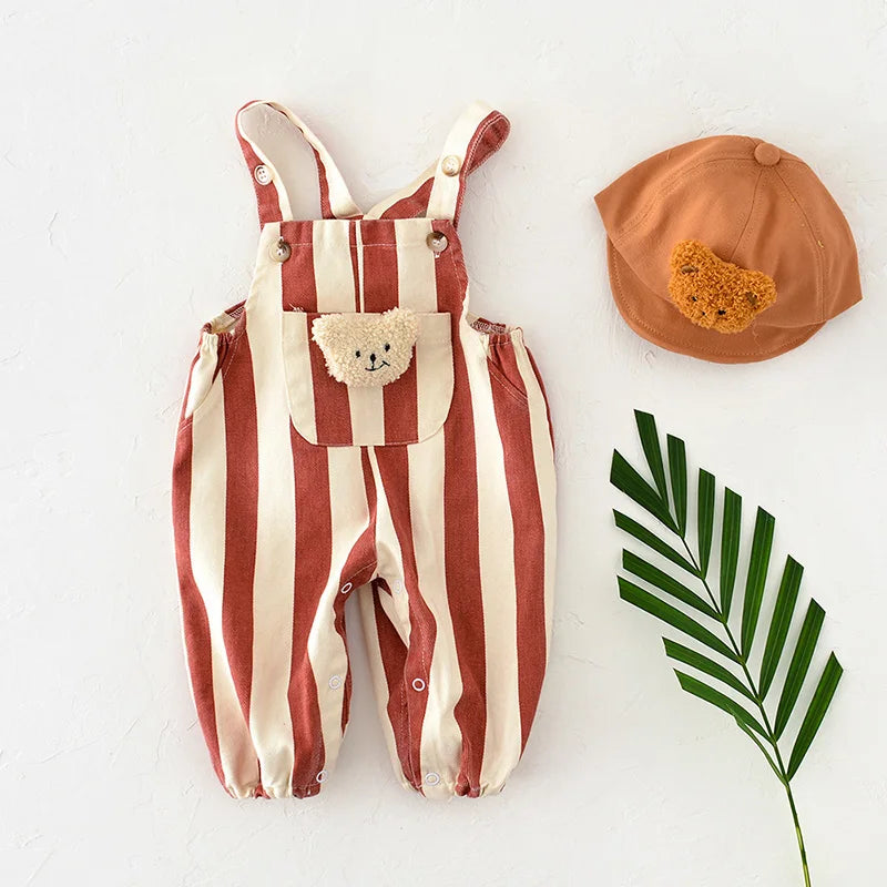 A striped baby romper in beige and terracotta with a bear decoration, next to an orange hat.