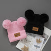 A pink knit baby beanie hat with black faux fur ears and a black beanie is shown next to some natural beauty products.