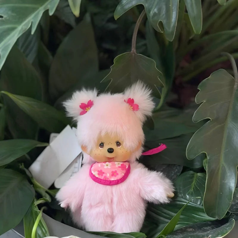 A pink fluffy bear plush toy with a stitched face and pink accents, set against green foliage.