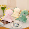 A pink and green dinosaur plush toy resting on a white table next to a mug and a book.