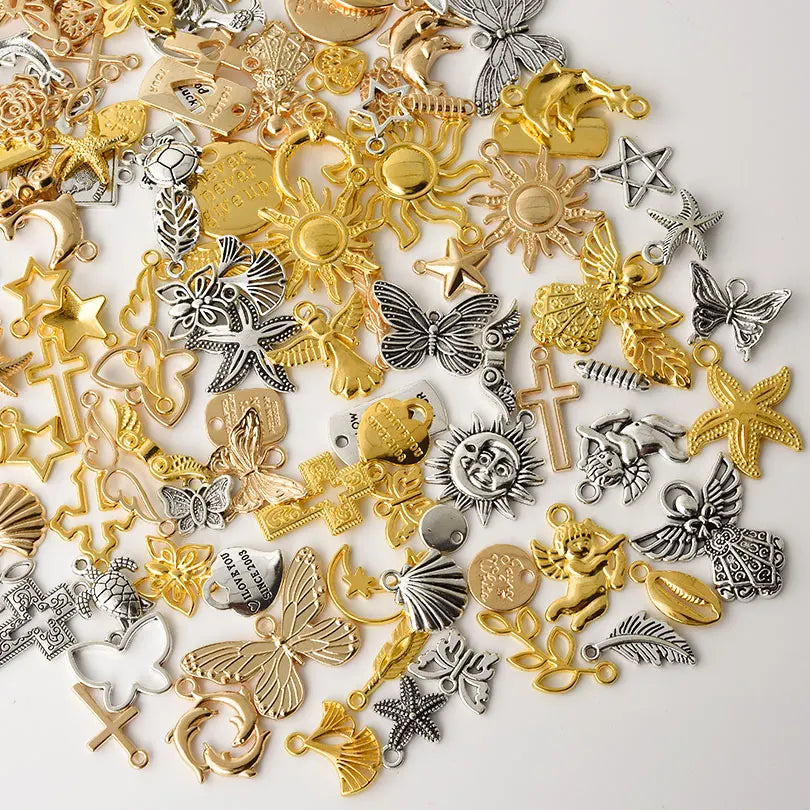 A collection of mixed metal charms including gold and silver stars, crosses, leaves, and butterflies for DIY jewelry making