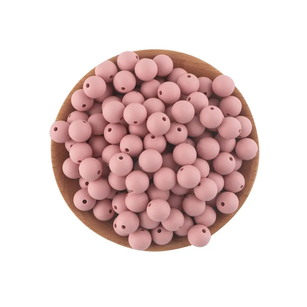 A pile of pink silicone round beads for jewelry making and DIY crafts arranged on a wooden surface.