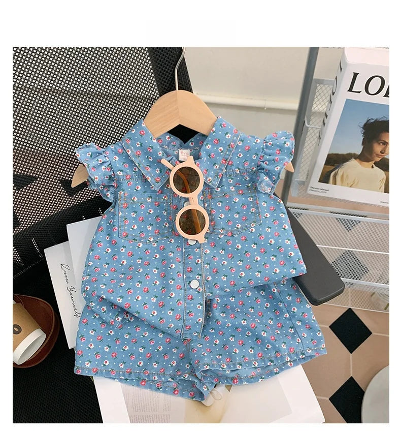 A light blue floral print girls' sleeveless shirt and shorts set displayed on a wooden hanger.