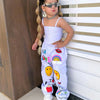 A young girl wearing a white two-piece outfit with suspender top and long pants featuring colorful graphics and sunglasses.