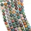 A collection of round loose natural India agate beads in various shades of green, purple, and brown.