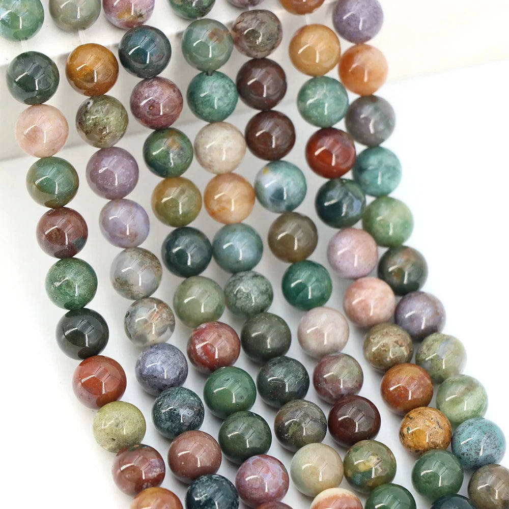 A collection of round loose natural India agate beads in various shades of green, purple, and brown.