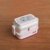 A pink miniature doll picnic lunch box with a lid featuring a small illustration of characters.