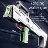 A white and black folding water gun is shown firing a stream of water in a dark, outdoor setting.