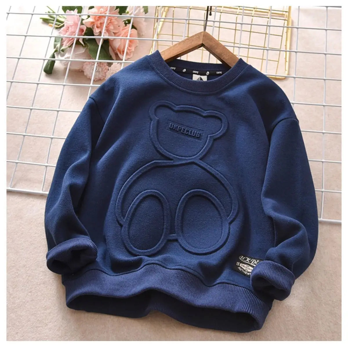 A navy blue kids cartoon bear pullover sweatshirt displayed on a hanger against a light background.
