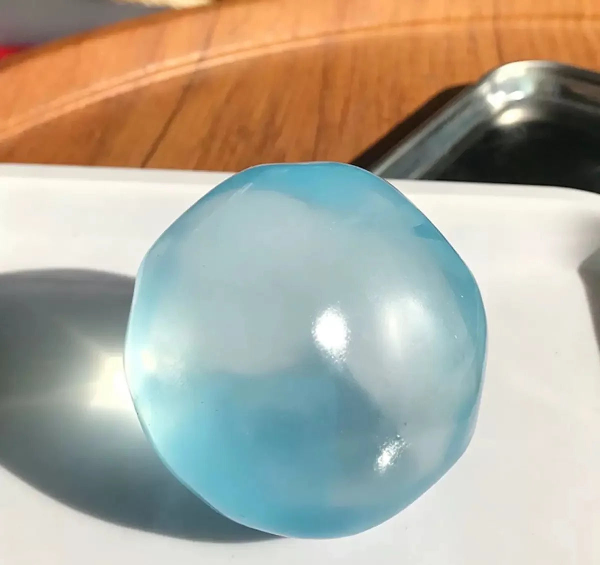 A translucent light blue squishy stress ball resting on a white surface.