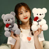 A young woman holds a white t-shirt and two teddy bears, one gray and one white, with a red rose.