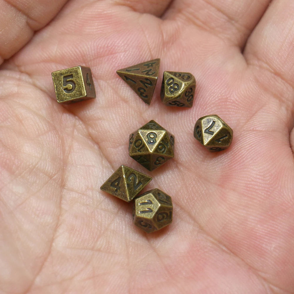 A hand holds a set of seven antique metal polyhedral dice, including a five-sided die and various other shapes.