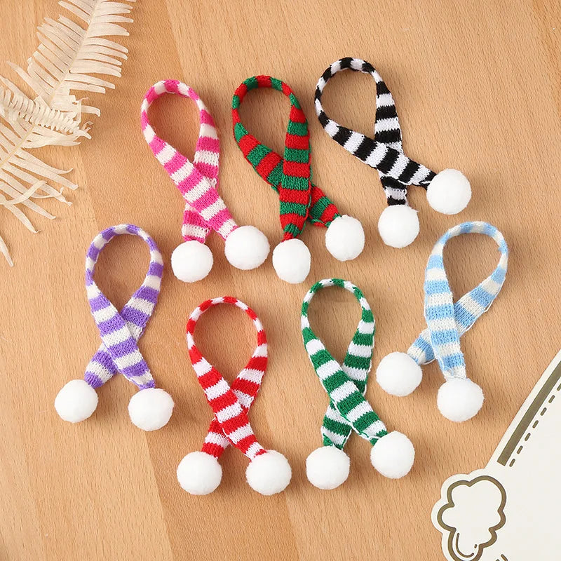 A set of mini knit Christmas hats and scarves in various colors like pink, green, purple, and blue on a wooden surface.