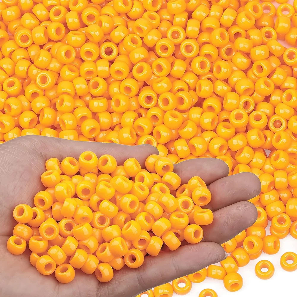 A hand holds a pile of small yellow pony beads for jewelry, braids, and crafts.