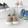 A collection of plaid slip-on toddler shoes in pink, black, and yellow checkered patterns displayed on a white surface.